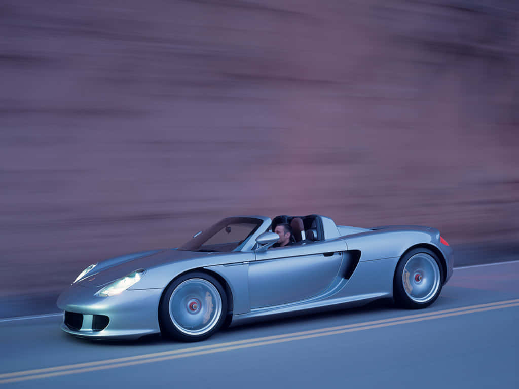 Striking Porsche Carrera Gt Roaring Along The Road Wallpaper