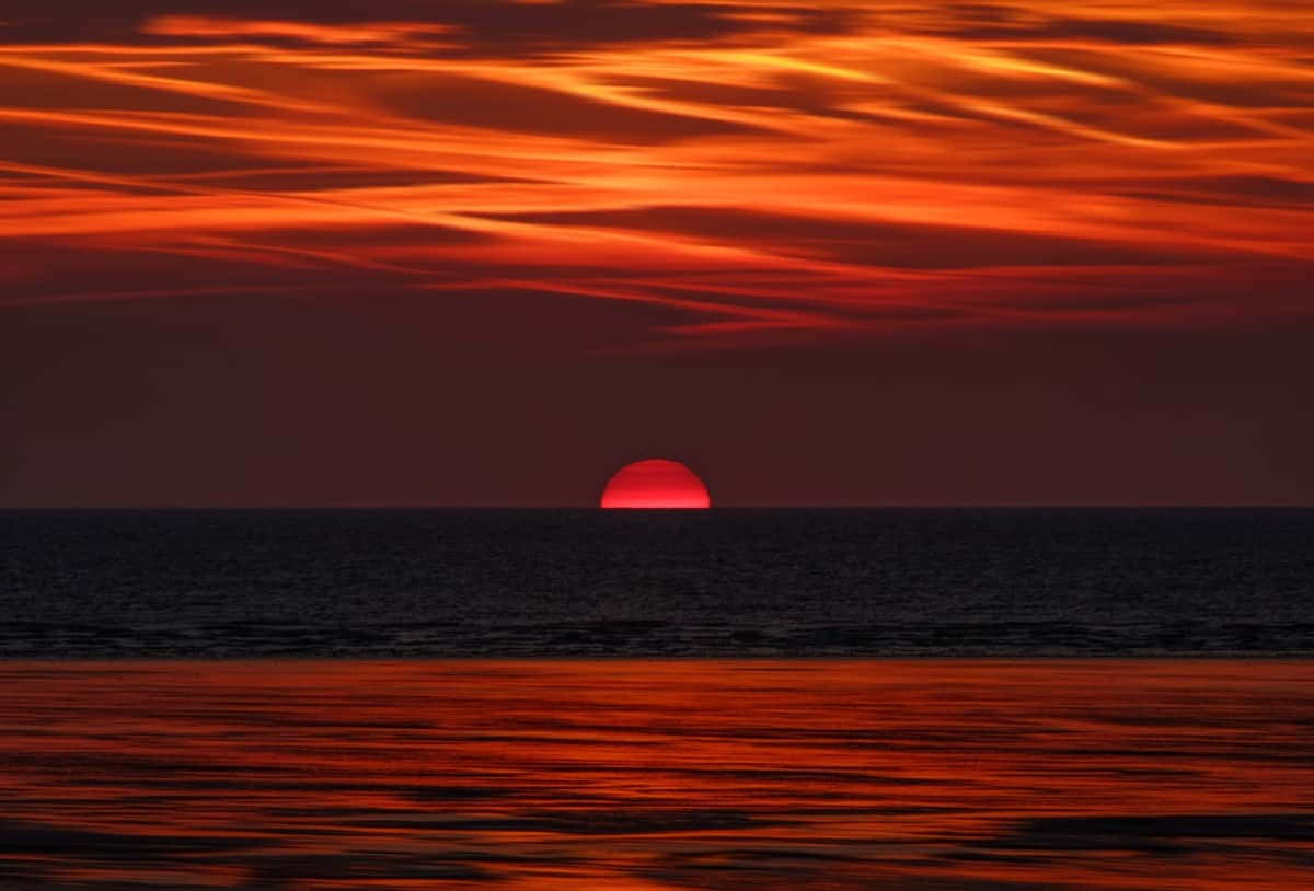 Stunning Red Sunset Sky Over Tranquil Waters Wallpaper