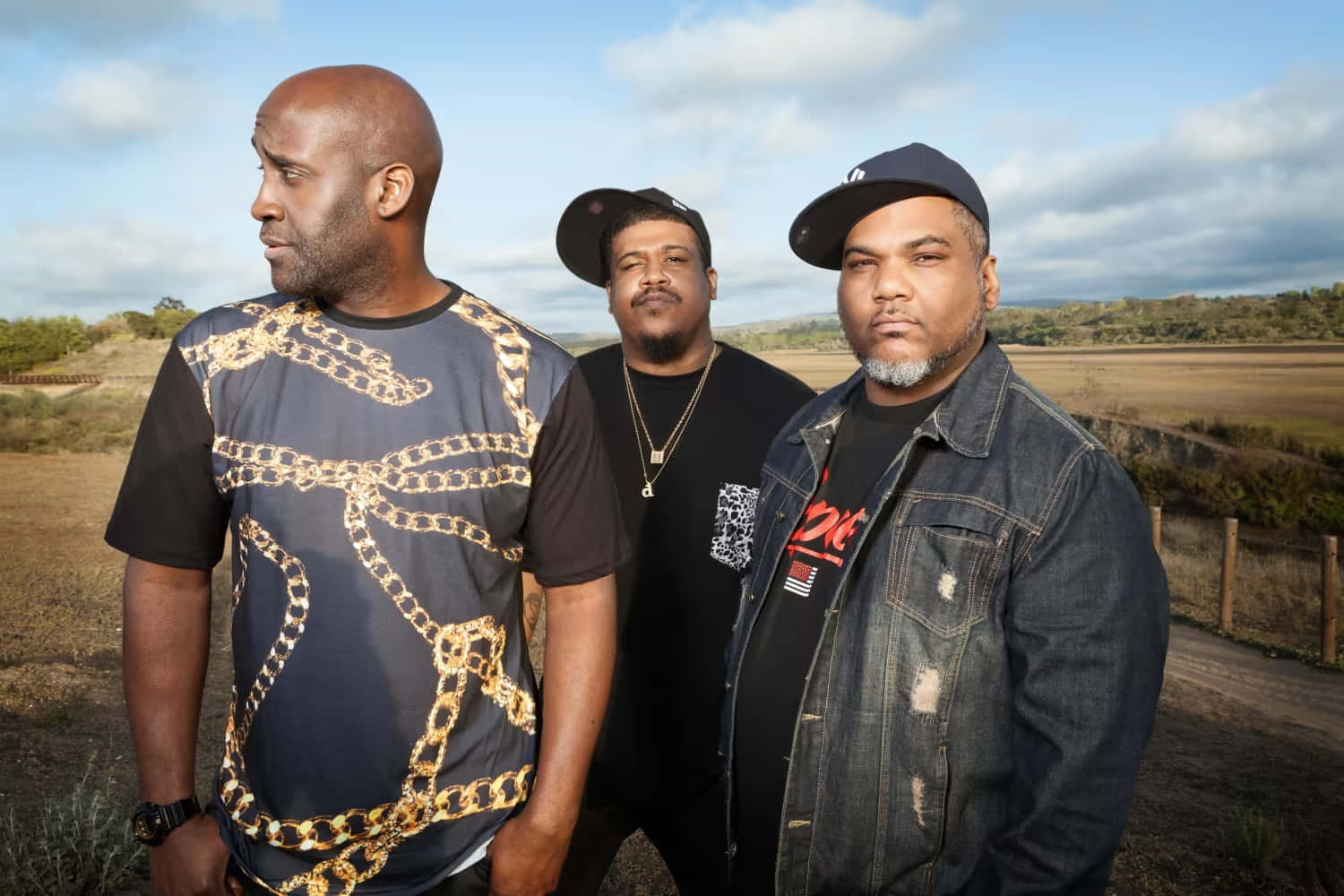 Three Men Standing In A Field With A Chain Necklace Wallpaper