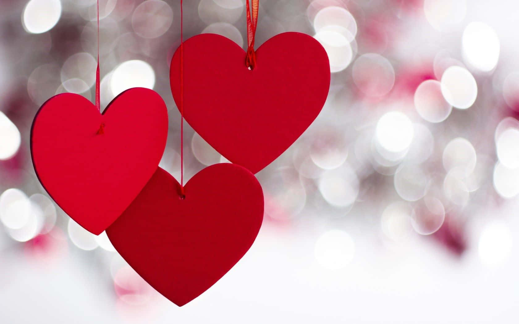 Three Red Hearts Hanging From Strings With A Bokeh Background Wallpaper