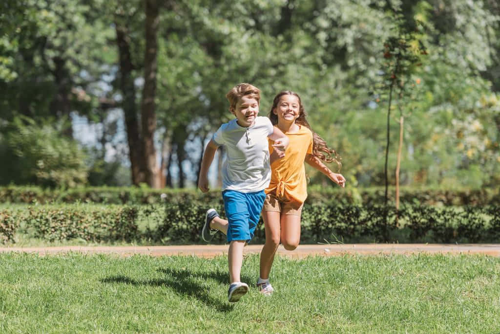 Two Adorable Kids Smiling In A Park Wallpaper