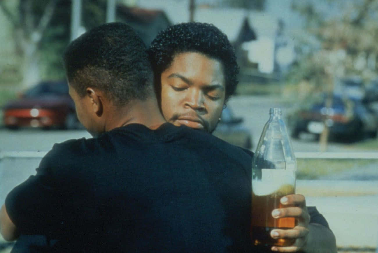 Two Men Hugging Each Other In Front Of A Building Wallpaper