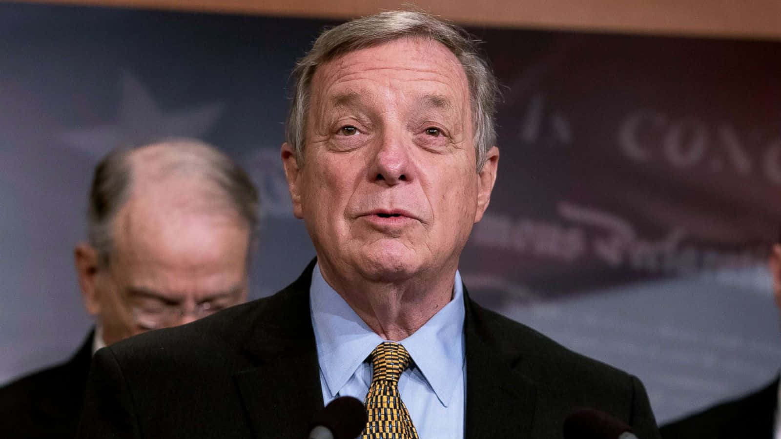 U.s. Senator Richard Durbin Speaking At A Press Conference Wallpaper