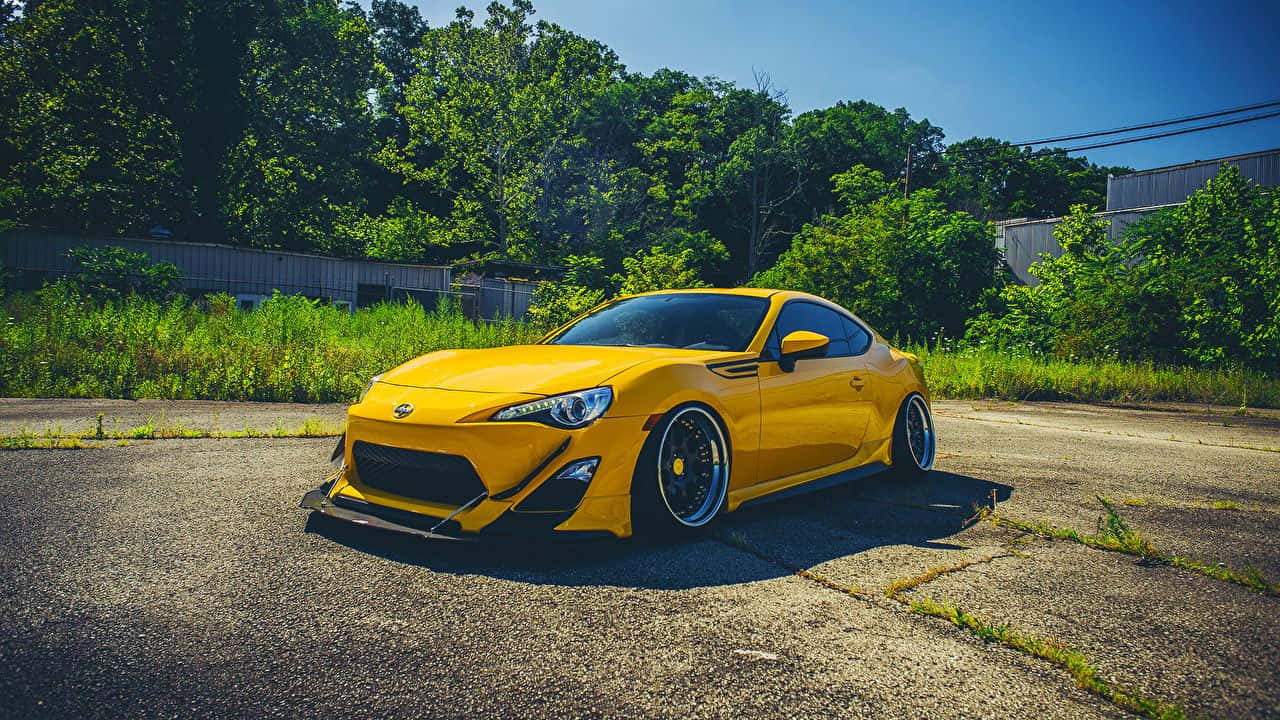 Vibrant Yellow Sports Car On Open Road In Nature Wallpaper