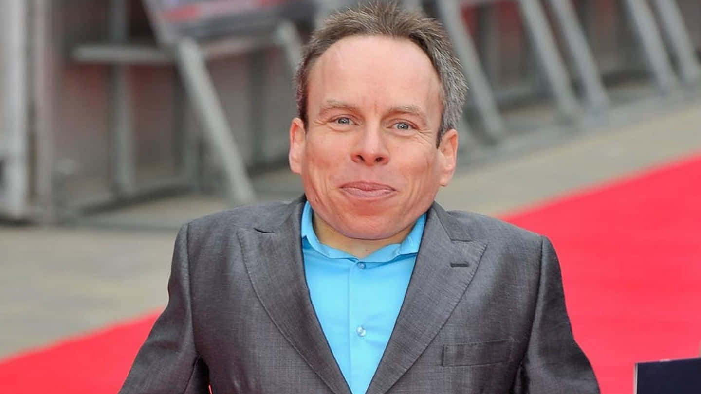 Warwick Davis Smiling During A Public Appearance Wallpaper