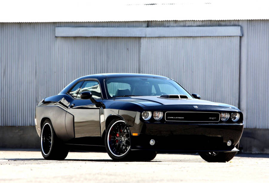 A Black Dodge Challenger Parked In Front Of A Building Wallpaper