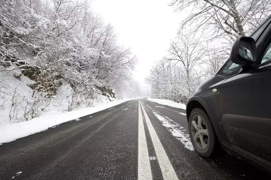 A Car Driving Through A Snowy Winter Road Wallpaper