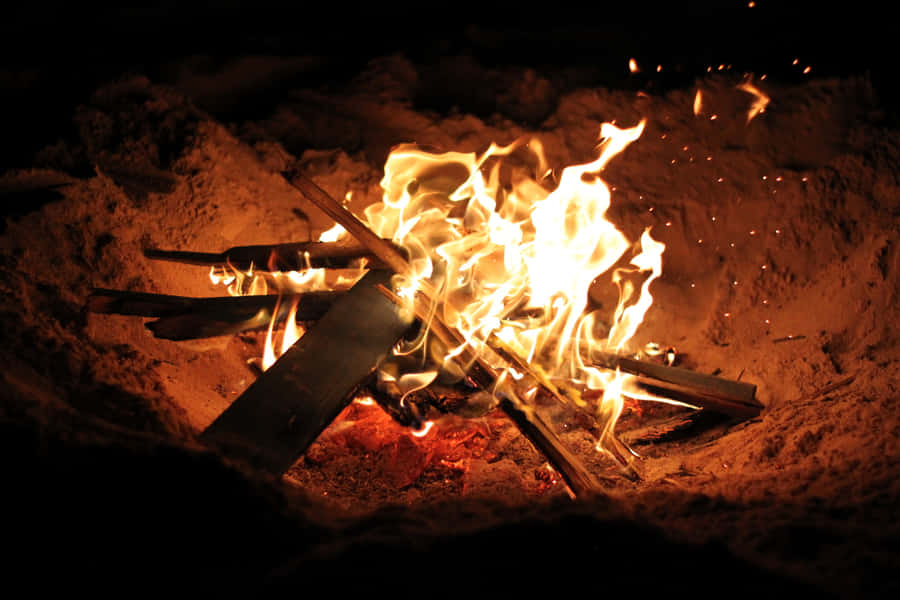 A Cozy Beach Bonfire Under The Starry Night Sky Wallpaper
