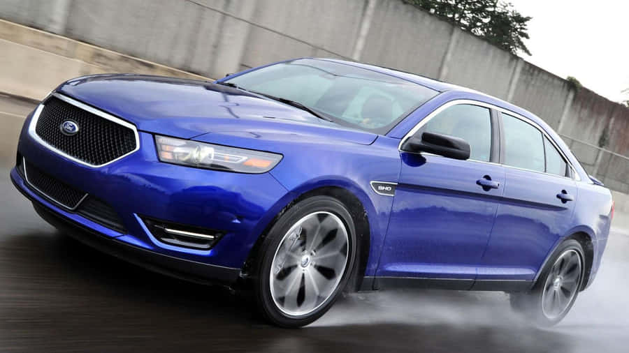 A Ford Taurus Moving On The Street At High Speed, Showcasing Its Sleek Design And Powerful Features. Wallpaper