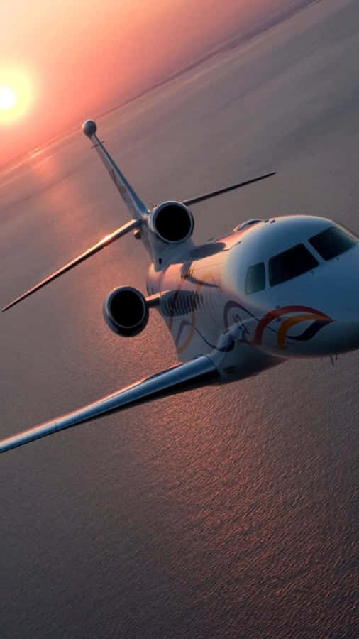 A Private Jet Flying Over The Ocean At Sunset Wallpaper