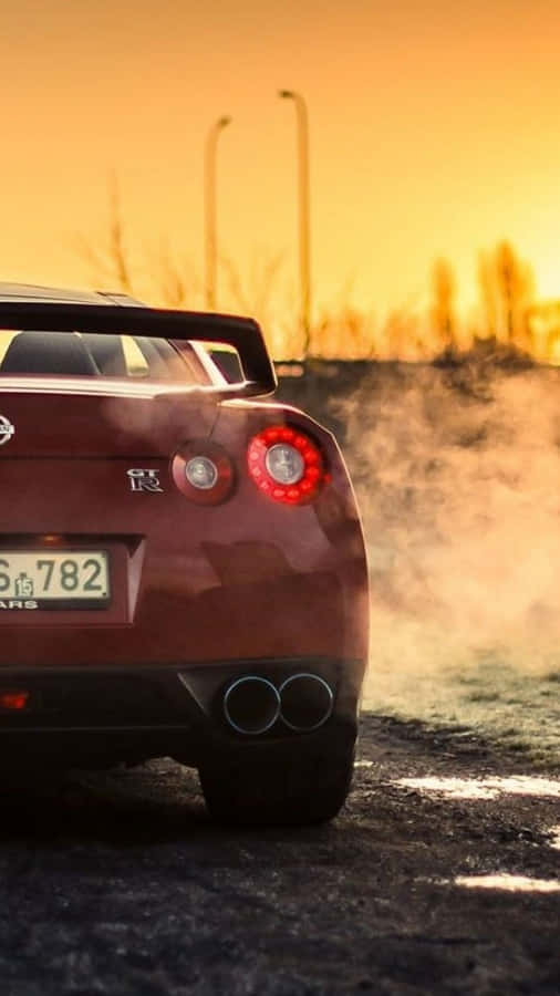 A Red Sports Car Is Driving Down The Road At Sunset Wallpaper