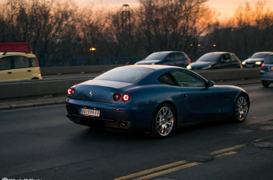 A Sleek Red Ferrari 612 Scaglietti Against A Scenic Countryside Backdrop. Wallpaper