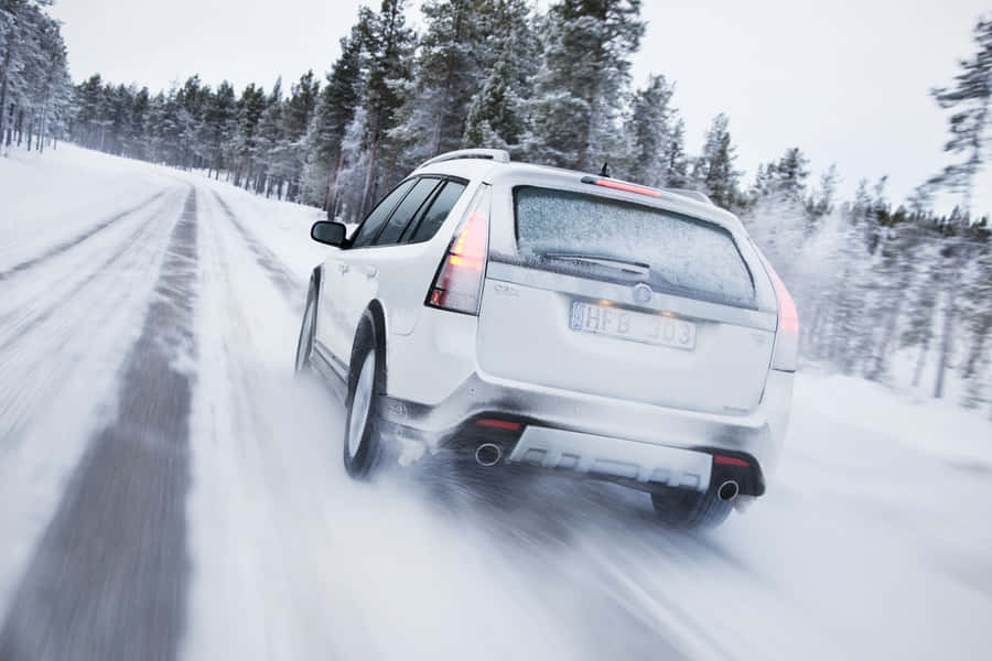 A Snowy Winter Road With A Car Driving Through The Picturesque Landscape Wallpaper