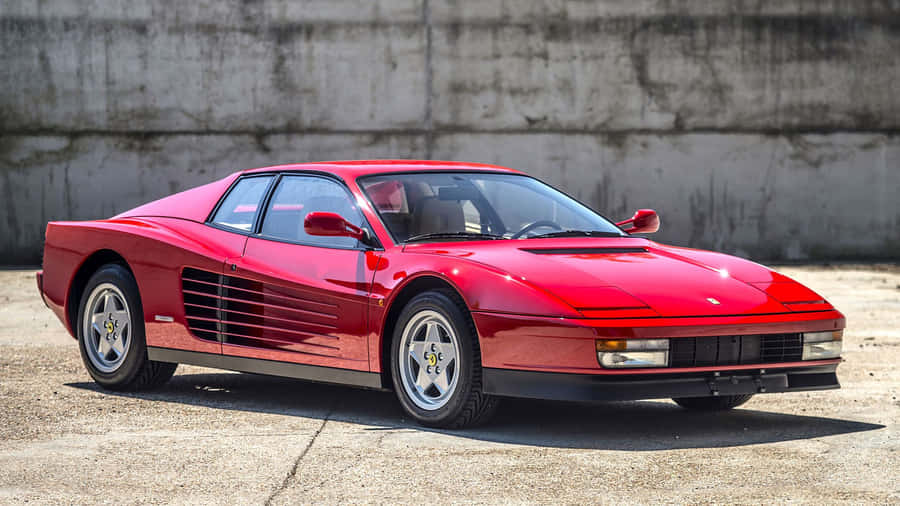 A Stunning Red 1984 Ferrari Testarossa Posed Against A Striking Cityscape Backdrop Wallpaper