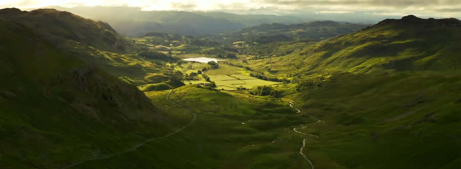 A View Of A Valley With A Stream And Mountains Wallpaper