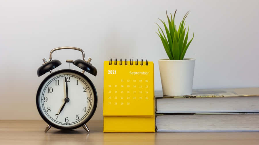 A Yellow Alarm Clock Sits Next To A Book And Plant Wallpaper