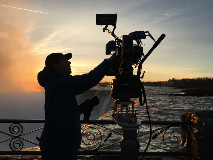 Cameraman Capturing Sunsetat Waterfall Wallpaper