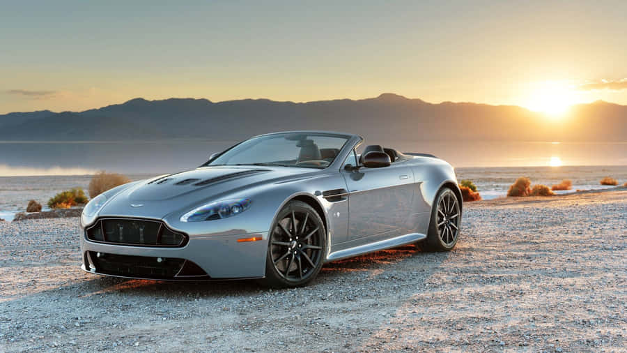 Caption: Aston Martin V12 Vantage Cruising On A Scenic Road Wallpaper