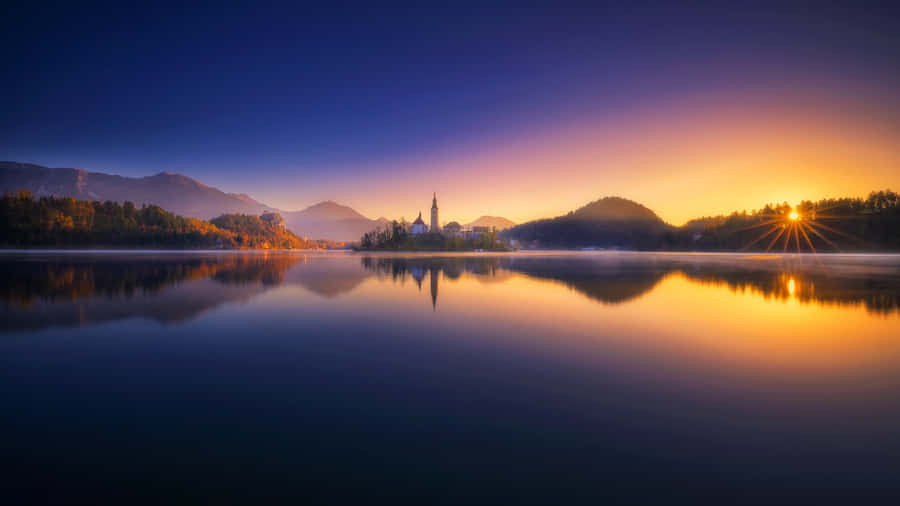 Caption: Breathtaking Sunset Over Lake Bled Panorama Wallpaper