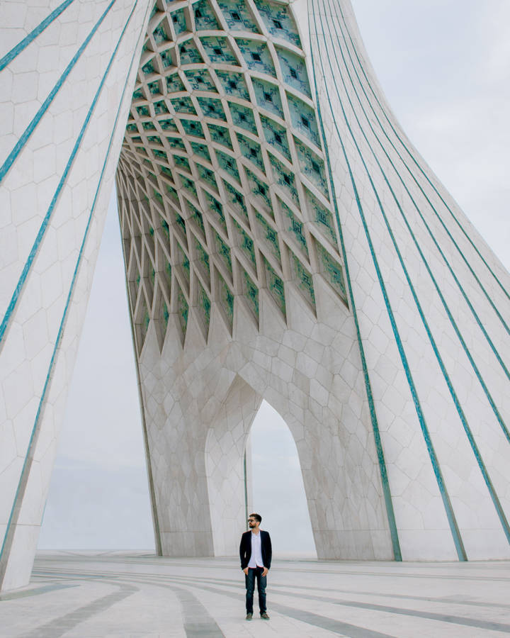 Caption: Man Standing In Front Of The Azadi Tower In Tehran, Iran Wallpaper