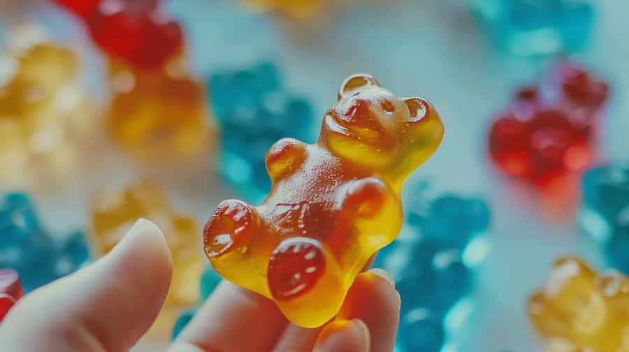 Colorful Gummy Bear Held In Fingers Wallpaper