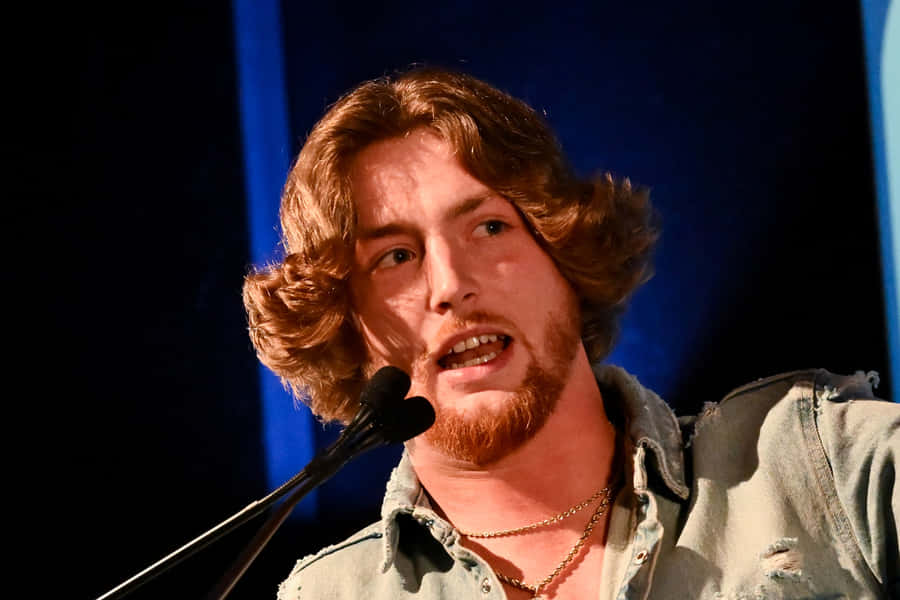 Country Singer Speakingat Microphone Wallpaper