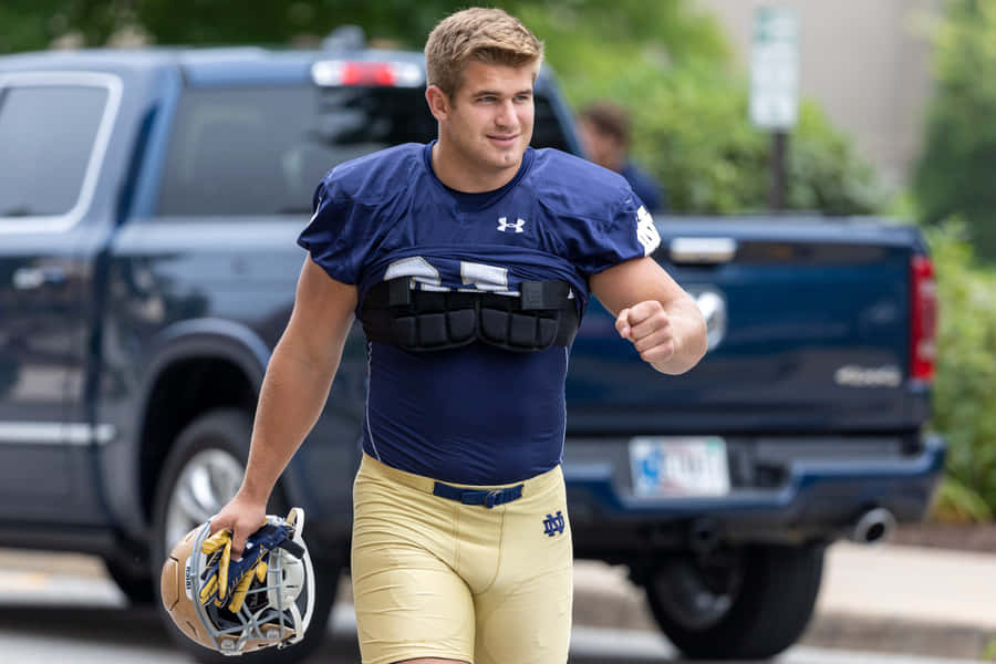 Football Player Walking With Helmetand Pads Wallpaper