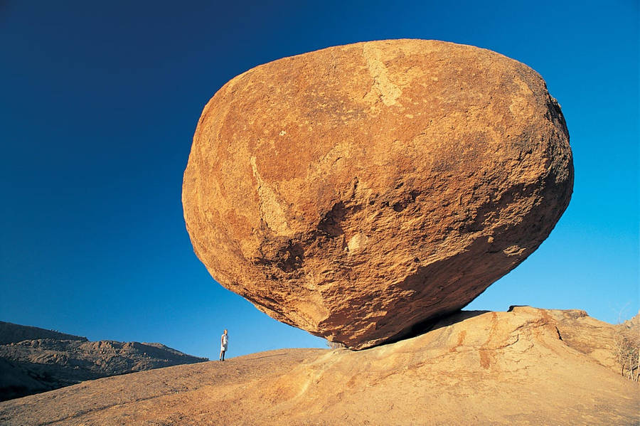 Man Standing Under Big Rock Wallpaper