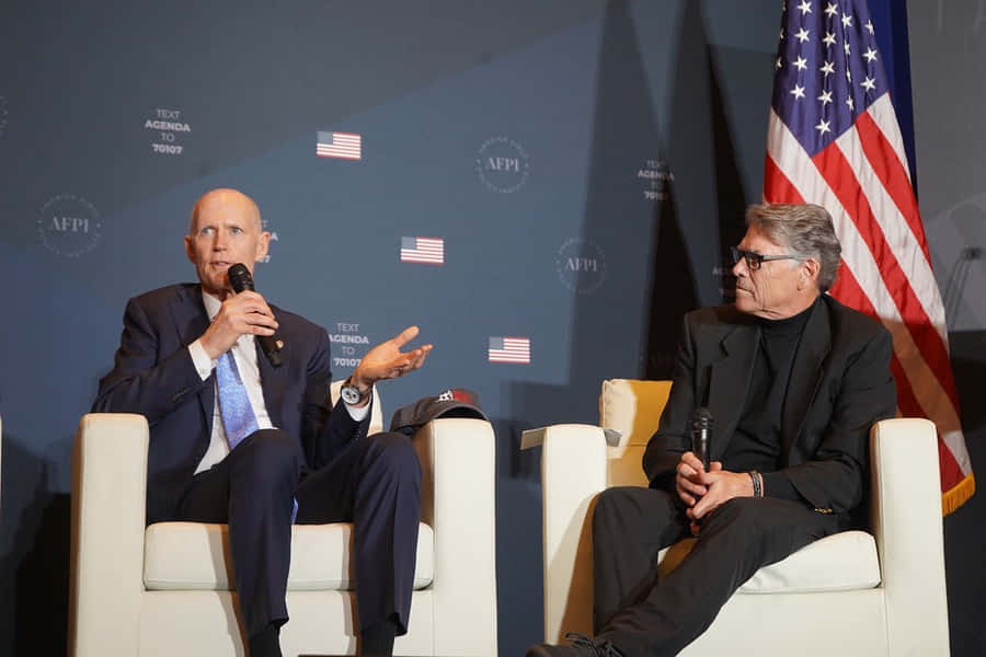 Rick Scott Delivering A Speech At The Afpi Summit Wallpaper