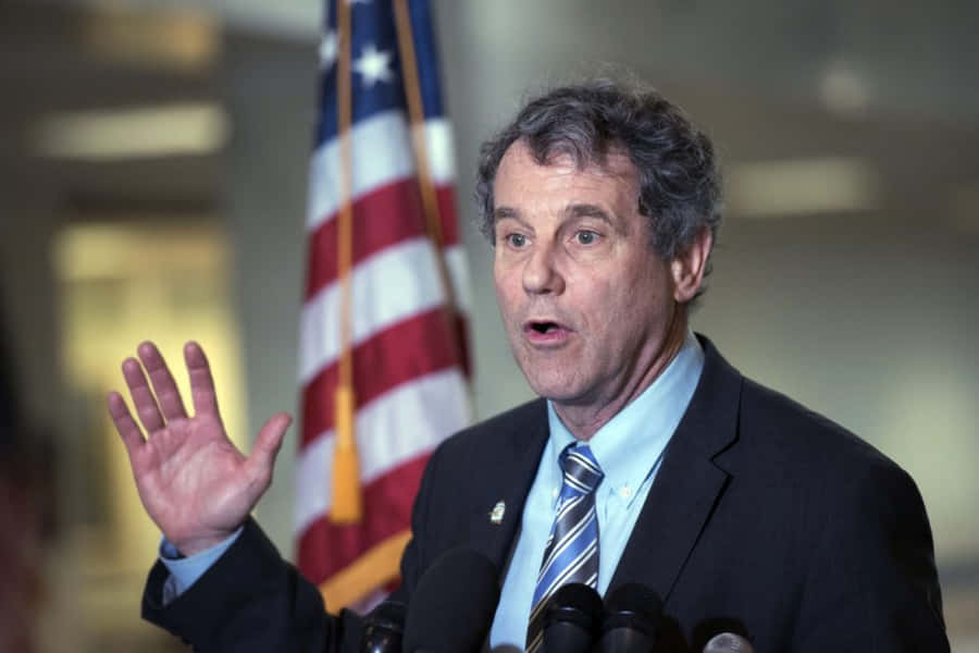 Sherrod Brown Proudly Standing Against The Backdrop Of The U.s. Flag Wallpaper