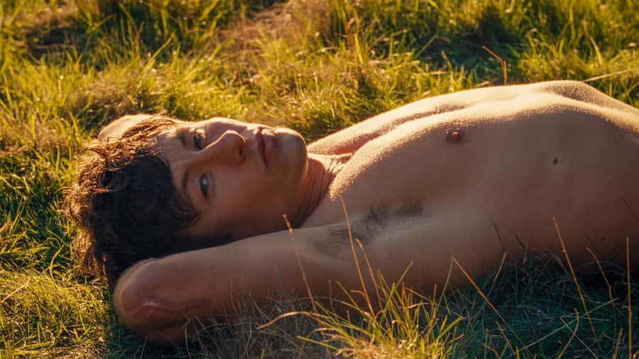 Shirtless Man Lyingin Grass During Golden Hour Wallpaper