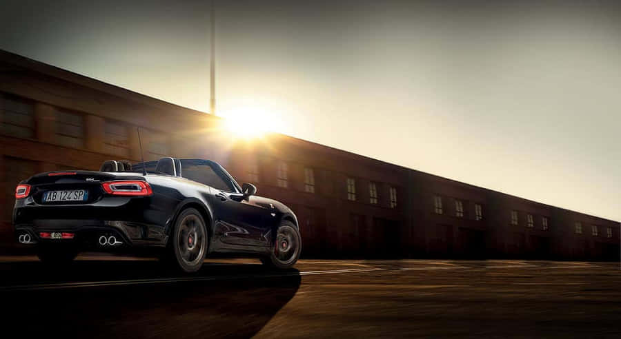 Sleek Fiat 124 Spider Cruising On The Open Road Wallpaper