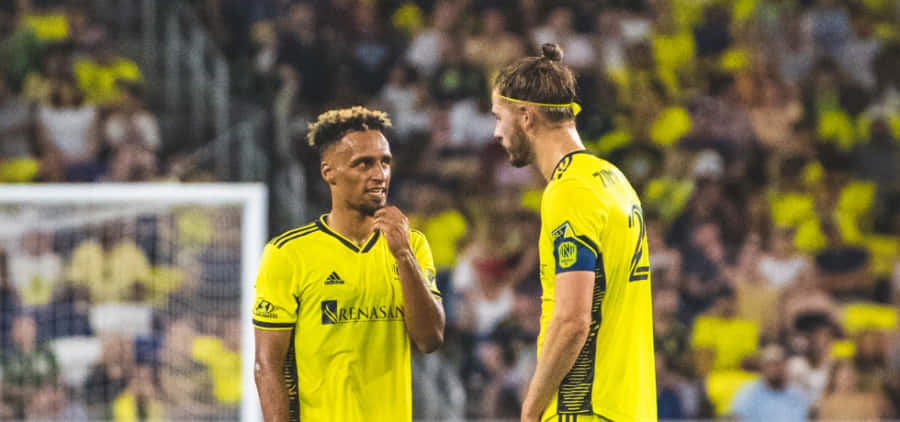 Soccer Players Discussing Strategy On Field Wallpaper