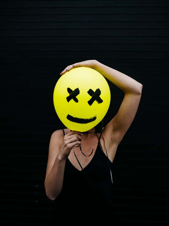 Woman Holding A Yellow Smiley Face Balloon Wallpaper