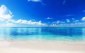 A Beach With Blue Water And Clouds Wallpaper