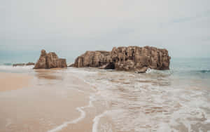 A Beach With Rocks And Waves On It Wallpaper