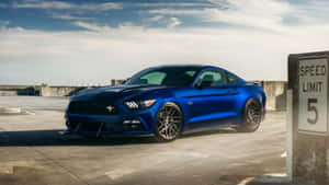 A Blue Ford Mustang Gt Parked In Front Of A Sign Wallpaper