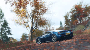 A Blue Sports Car Driving Down A Road In Autumn Wallpaper