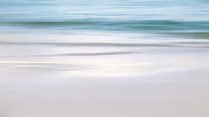 A Blurry Image Of A Beach With Water And Sand Wallpaper