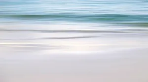 A Blurry Image Of A Beach With Water And Sand Wallpaper