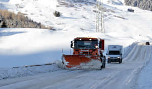 A Bright Orange Snowplow Clears The Icy Road During A Winter Storm Wallpaper