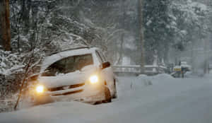 A Car Driving On A Snowy Road In A Winter Landscape Wallpaper