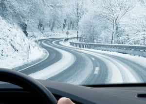 A Car Driving Through A Snowy Road During Winter Wallpaper