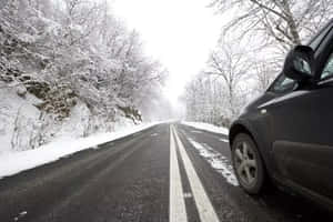 A Car Driving Through A Snowy Winter Road Wallpaper