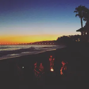 A Cozy Beach Campfire Under The Starry Night Sky Wallpaper