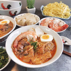 A Delicious Bowl Of Curry Laksa Surrounded By Fresh Ingredients Wallpaper