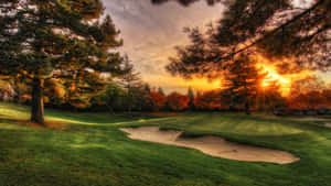 A Golfer Swings His Club With A Beautiful Golf Course In The Background. Wallpaper