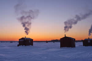 A Group Of Adventurous Ice Anglers In Action, Drilling Holes And Preparing For A Day Of Ice Fishing On A Frozen Lake Wallpaper