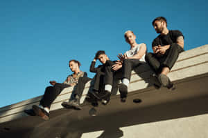 A Group Of Men Sitting On A Ledge Wallpaper