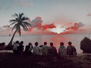 A Group Of People Sitting On The Beach Watching The Sunset Wallpaper